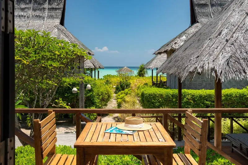 Terrasse en bois avec table et chaises donnant sur une végétation luxuriante et la mer.