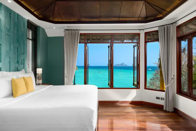 Chambre lumineuse avec un lit blanc et une vue sur la mer.