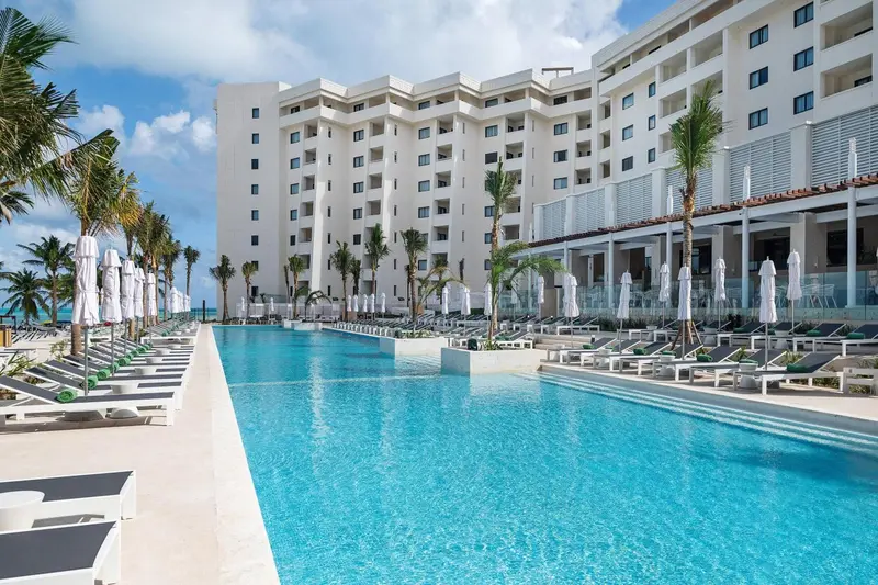 Vue d'une piscine turquoise devant un bâtiment blanc et des palmiers.