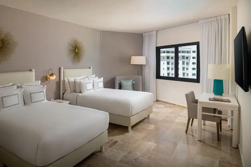 Une chambre lumineuse avec deux lits et un bureau près de la fenêtre.