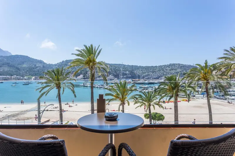 Une table et des chaises sur un balcon offrent une vue sur une plage et un port de plaisance.