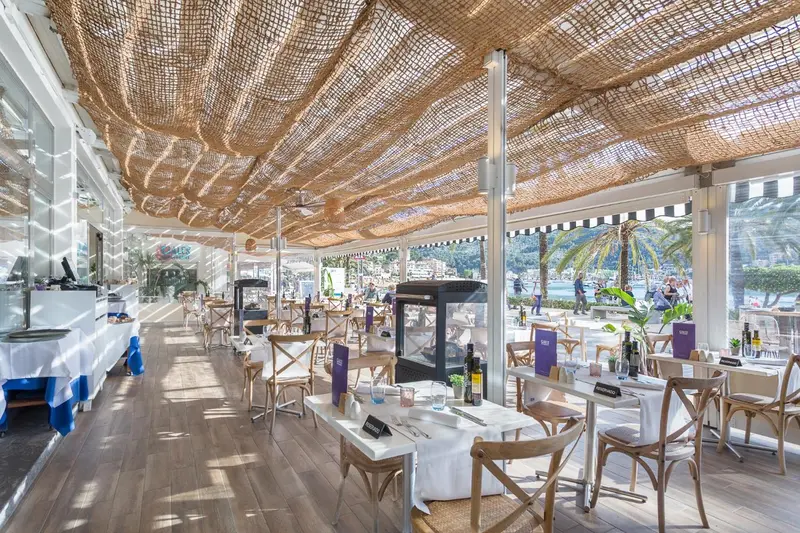 Une salle à manger lumineuse avec des tables dressées et une vue sur la mer.