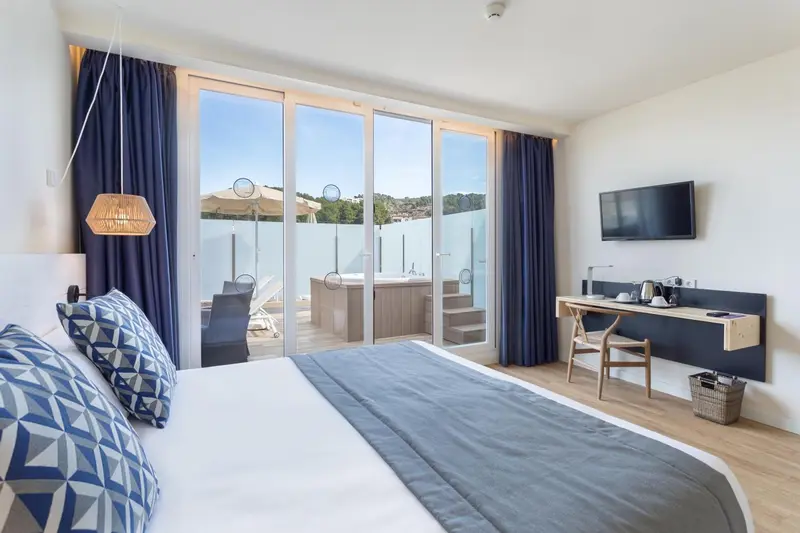 Chambre lumineuse avec un grand lit donnant sur une terrasse et un jacuzzi.