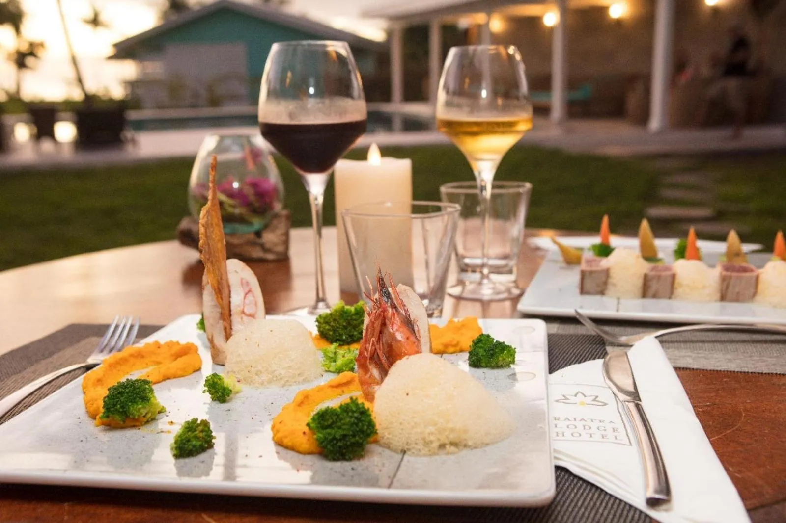 Une table est dressée avec des plats raffinés et des verres de vin, éclairés par une bougie.