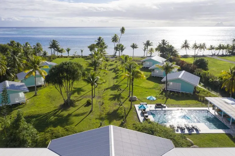 Vue aérienne d'un ensemble de bungalows turquoise au milieu d'une végétation luxuriante, face à la mer.
