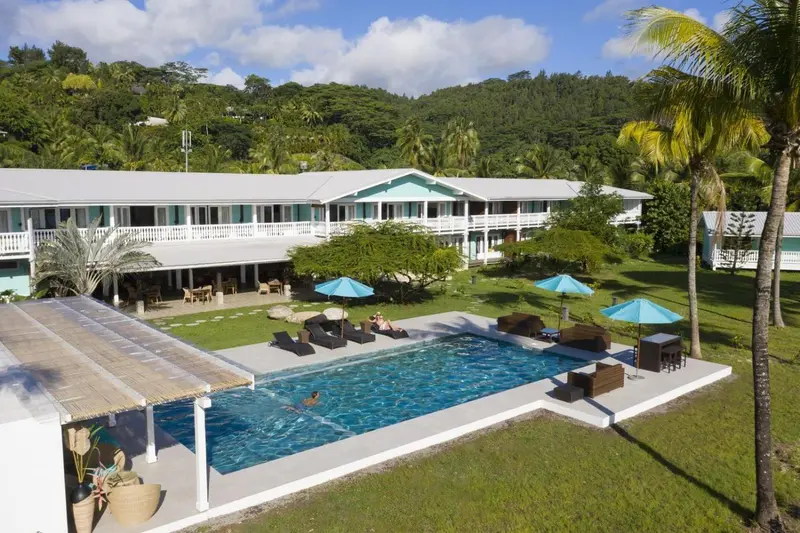 Vue aérienne d'une piscine entourée d'un jardin tropical et d'un bâtiment blanc.