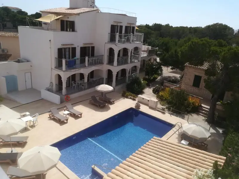 Bâtiment blanc à deux étages avec des balcons et une piscine en contrebas.