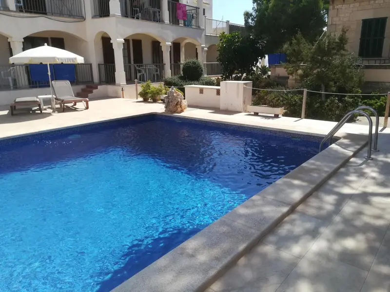 Une piscine rectangulaire avec des transats et des parasols sur une terrasse ensoleillée.