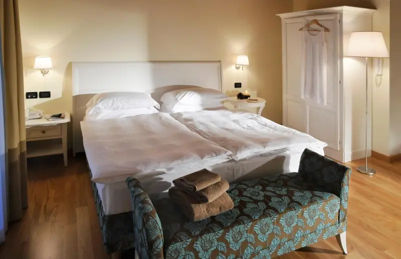 Une chambre lumineuse avec un grand lit et un banc au pied du lit.