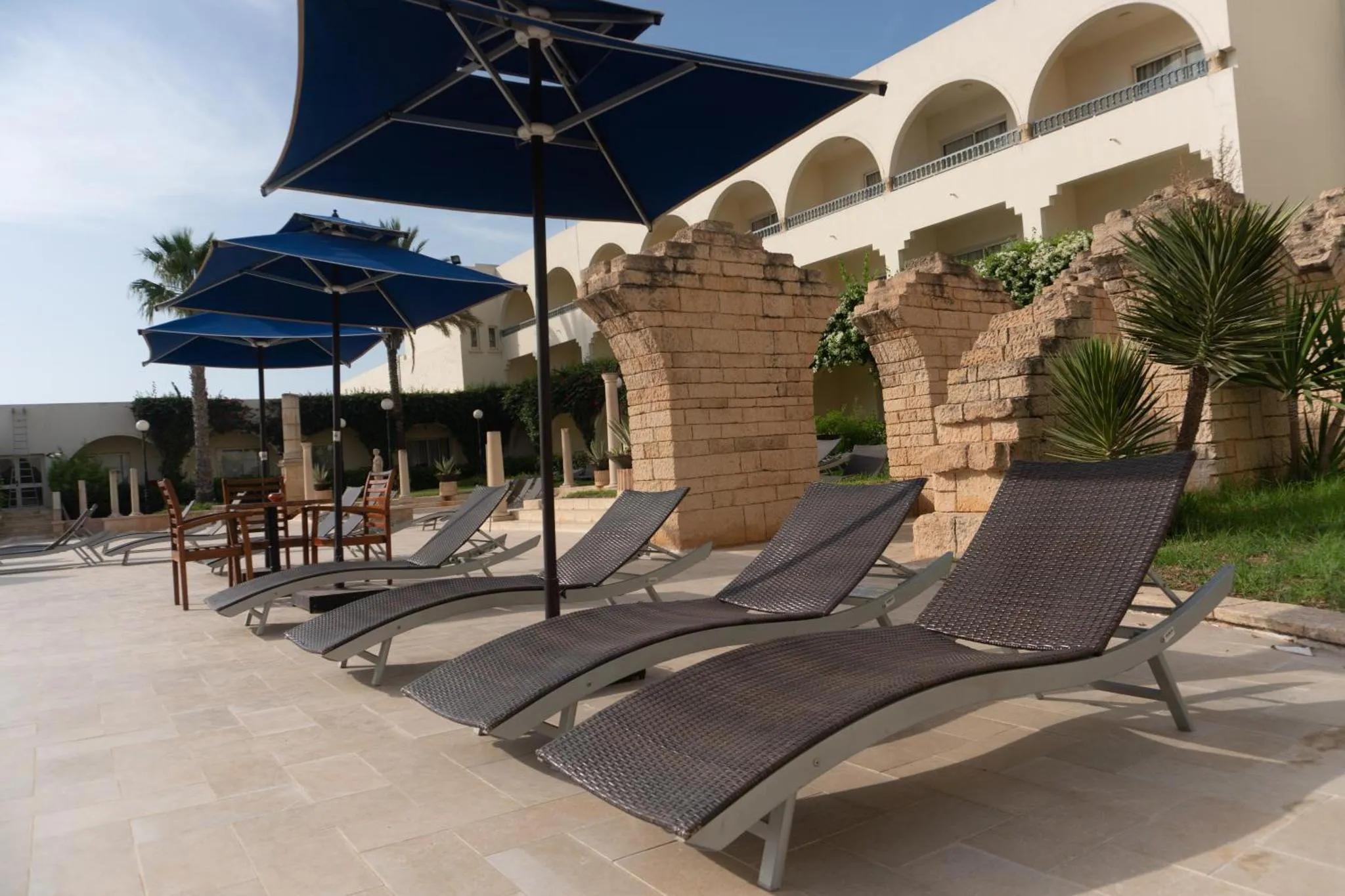 Transats et parasols sur une terrasse ensoleillée près d'une architecture en pierre.