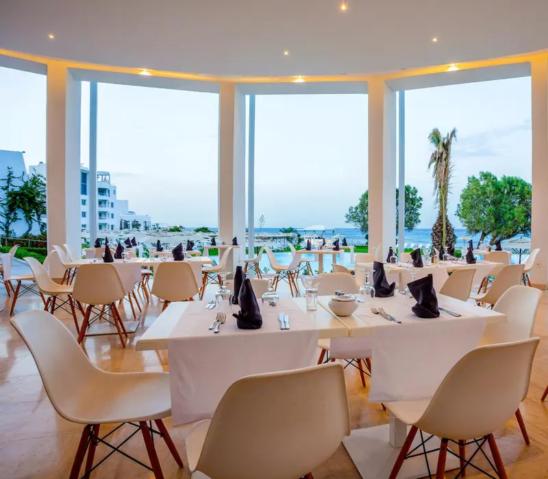 Une salle lumineuse avec des tables dressées face à la mer.