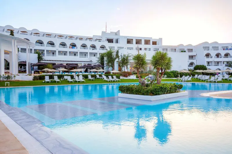 Vue d'un hôtel blanc avec une piscine et des transats.