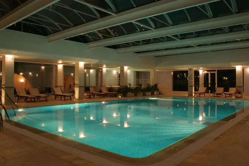 Une piscine intérieure illuminée avec des chaises longues sur le bord.