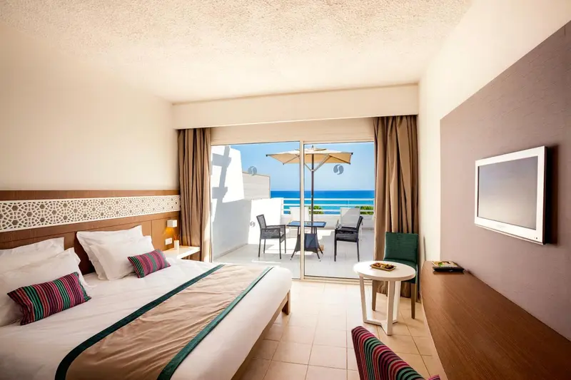 Une chambre lumineuse avec un grand lit donnant sur une terrasse et la mer.