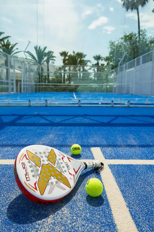 Raquette de padel et balle jaune sur terrain bleu.