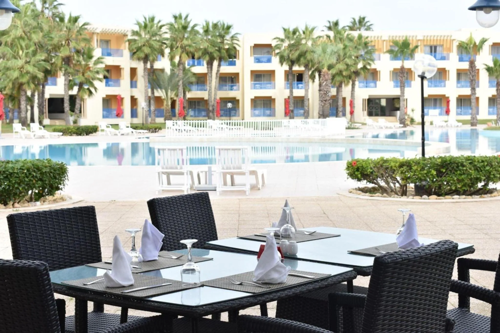 Tables de restaurant en extérieur avec vue sur une piscine et des palmiers.