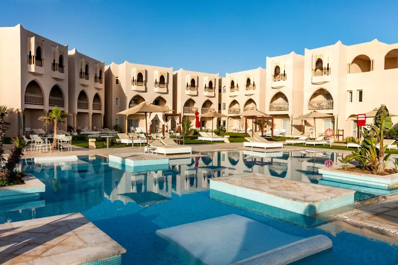 Bâtiment beige à plusieurs étages avec des arcades, surplombant une piscine et un espace de détente.