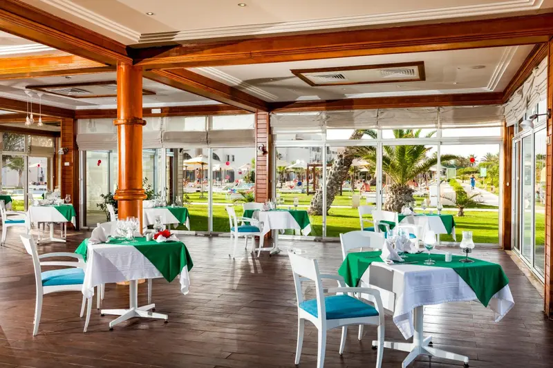 Une salle à manger lumineuse avec des tables dressées et vue sur une pelouse verdoyante.