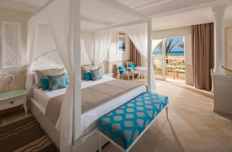 Une chambre lumineuse avec un grand lit à baldaquin et vue sur la mer.
