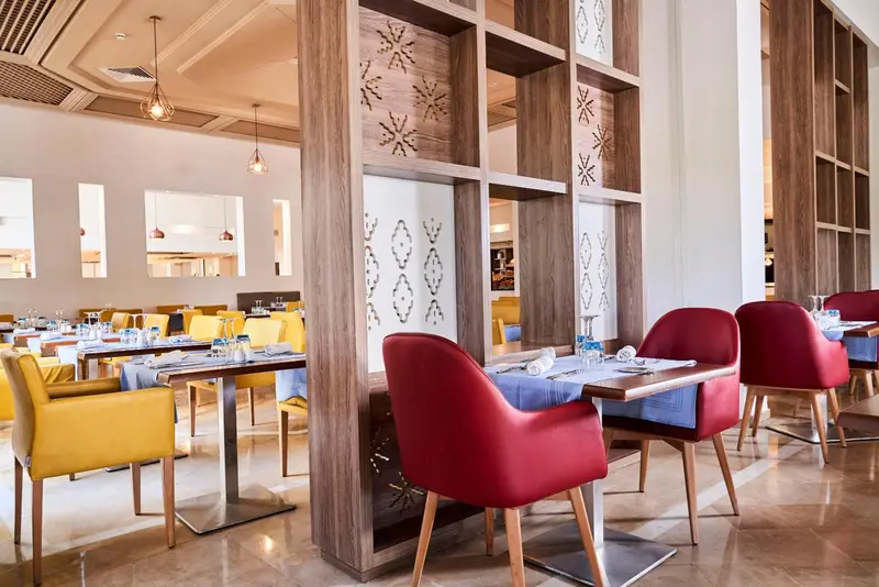 Une salle de restaurant lumineuse avec des tables dressées et des chaises colorées.