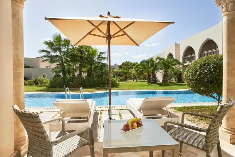 Terrasse avec transats et table basse près d'une piscine.