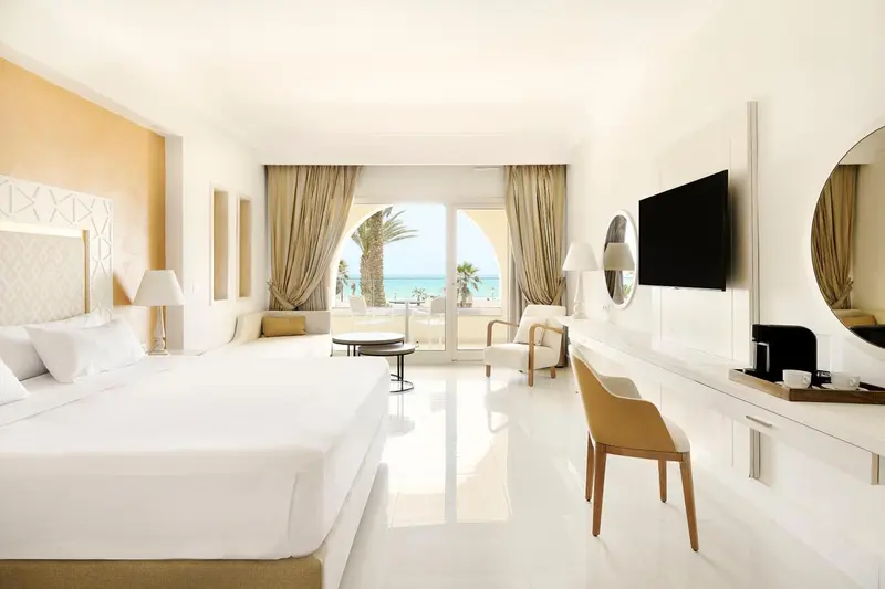 Chambre lumineuse avec un grand lit et vue sur la mer.