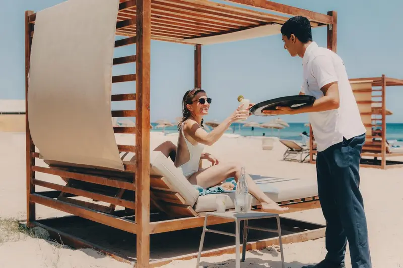 Une personne allongée sur un lit de plage reçoit un service de boissons.
