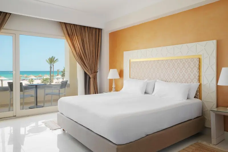 Chambre lumineuse avec un grand lit et vue sur la mer.