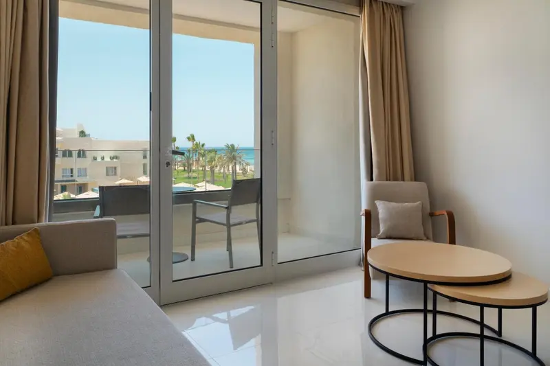 Espace de détente lumineux avec canapé et fauteuil près d'une baie vitrée donnant sur une terrasse.