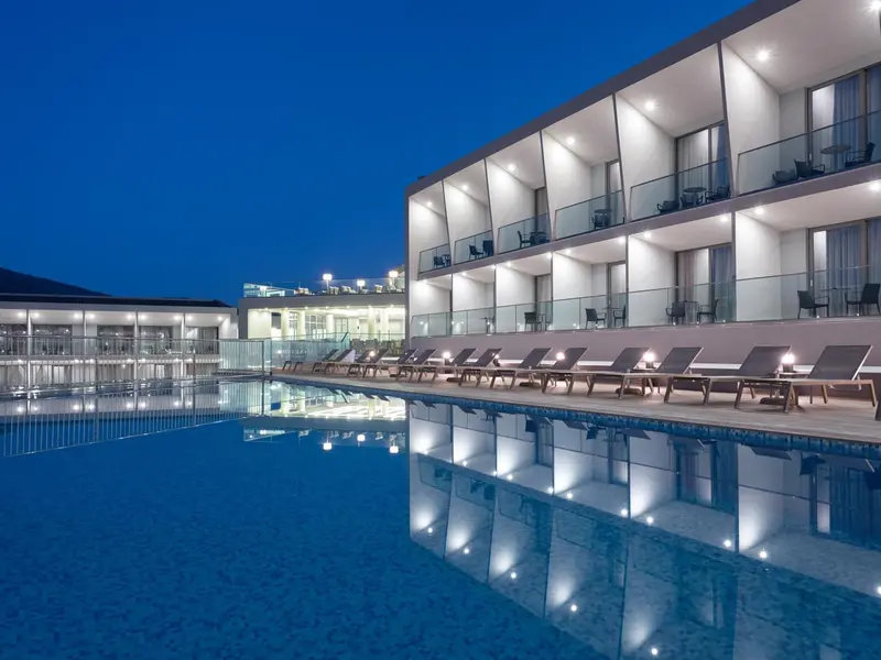 Bâtiment moderne éclairé au bord d'une piscine la nuit.