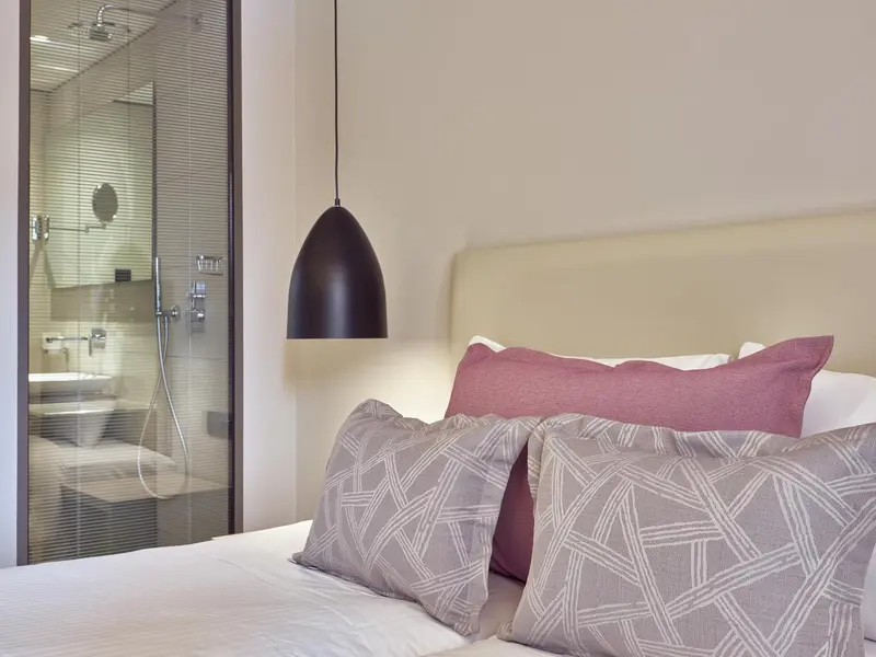 Un lit avec des oreillers est devant une paroi vitrée donnant sur une salle de bain.