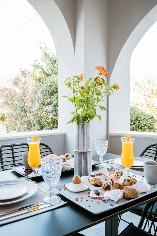 Une table est dressée avec un petit-déjeuner sur une terrasse ombragée.