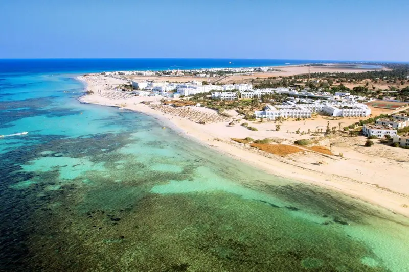 Vue aérienne d'une plage de sable blanc bordée d'eaux turquoise et d'une côte rocheuse.