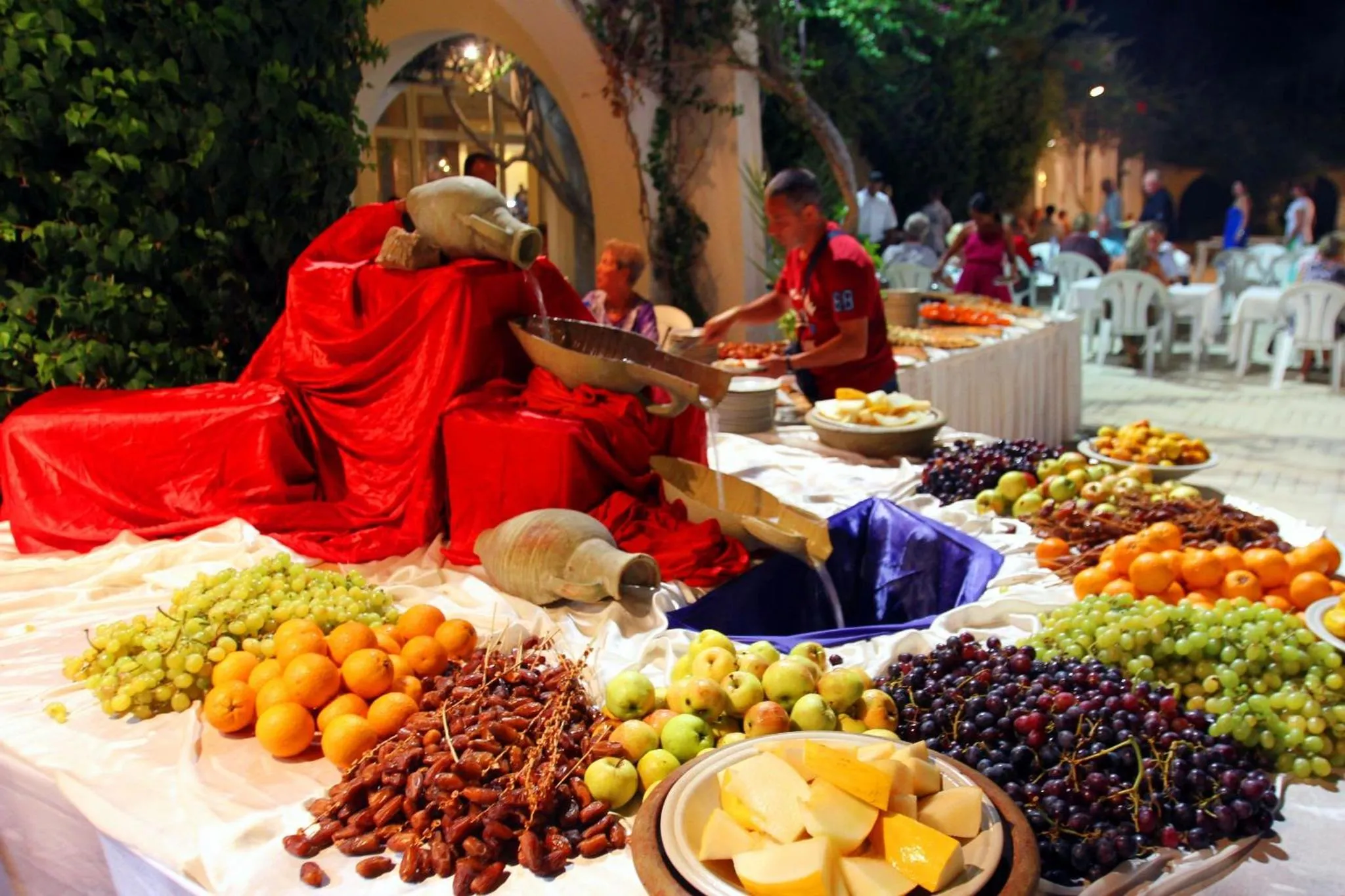 Un buffet de fruits et de pâtisseries est présenté sur une table décorée en extérieur.