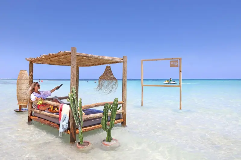 Une personne se relaxe sur un lit de plage ombragé face à la mer.