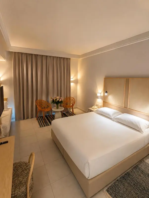 Une chambre d'hôtel lumineuse avec un grand lit et deux fauteuils.