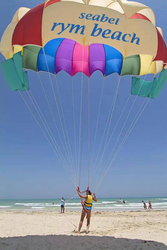 Une personne est attachée à un parachute coloré au-dessus d'une plage ensoleillée.