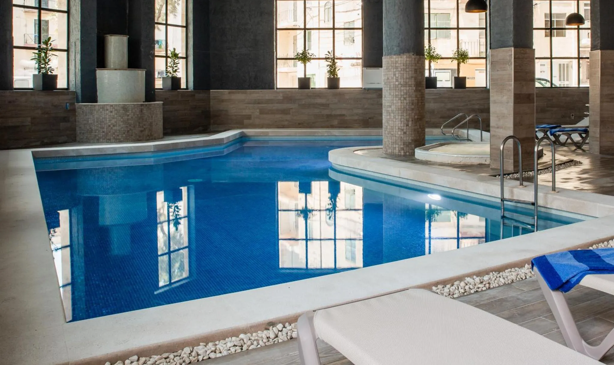 Une piscine interieure rectangulaire avec des transats blancs sur le bord.
