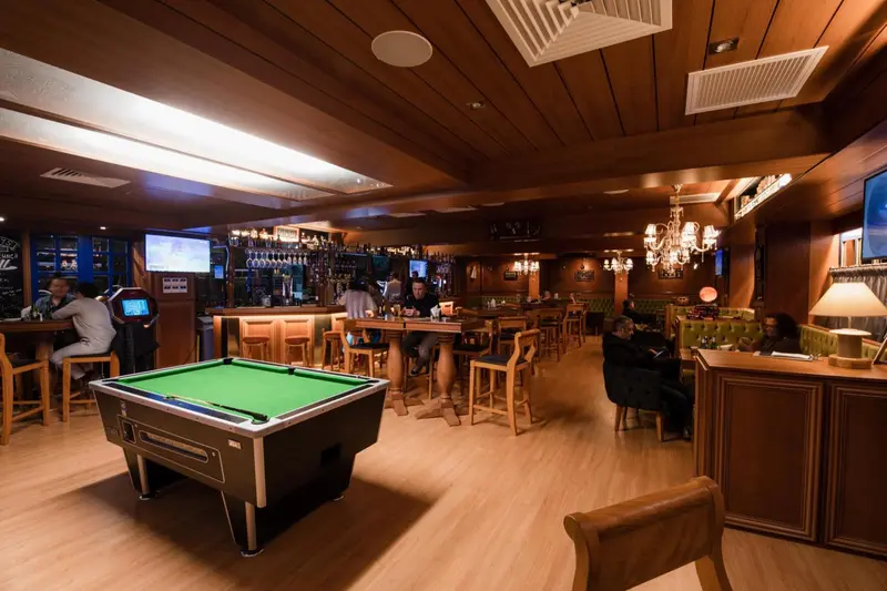 Un bar chaleureux avec un billard vert et des clients assis au comptoir.