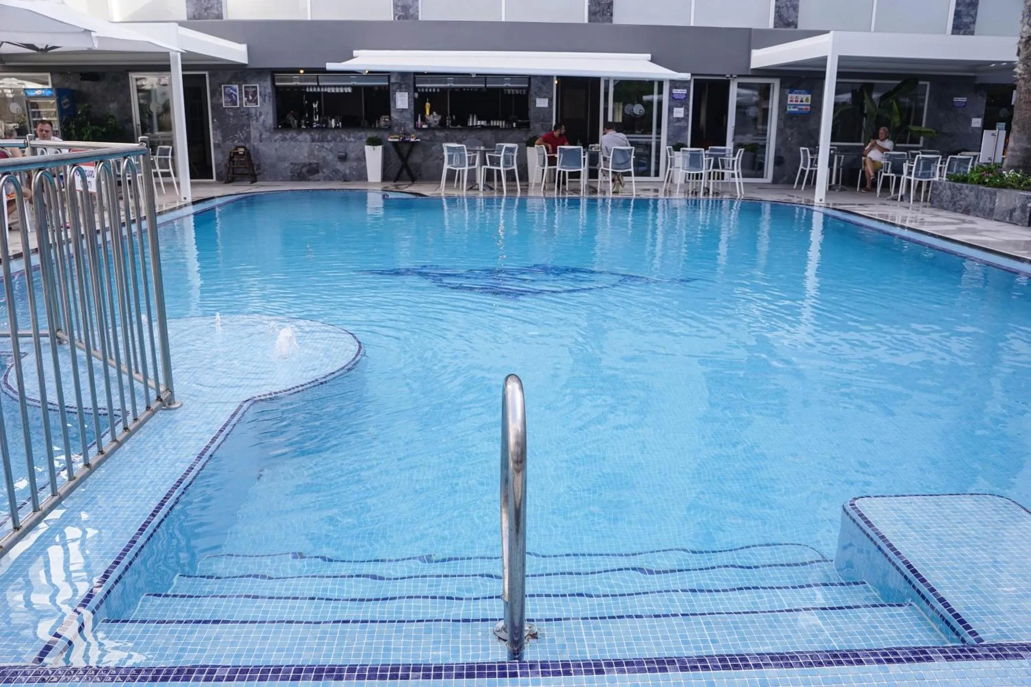 Une piscine rectangulaire avec des marches et des personnes assises sur des chaises longues.