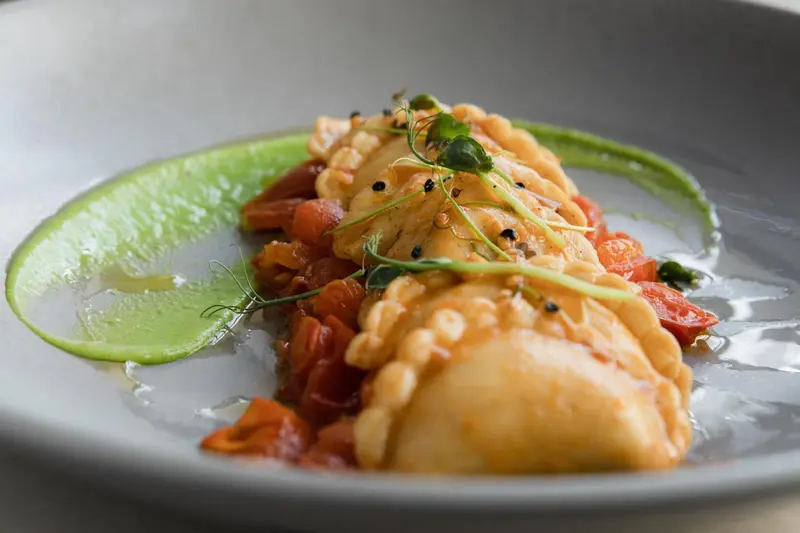 Assiette de raviolis aux couleurs vives, servis avec une sauce verte et des herbes fraîches.