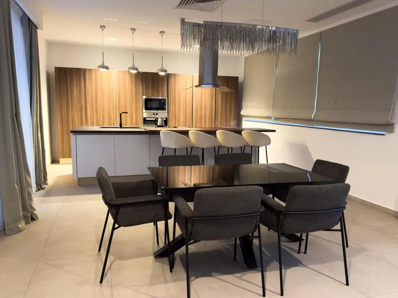 Une salle à manger lumineuse avec une cuisine moderne en fond.