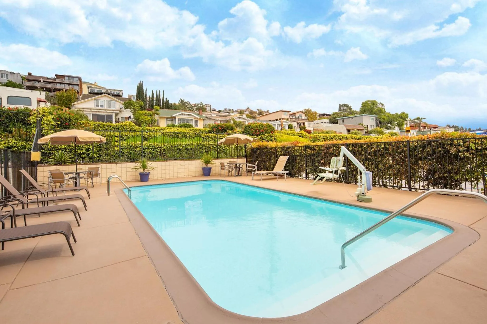 Une piscine rectangulaire avec des transats et des parasols, entourée d'une végétation luxuriante et d'une vue sur la mer.