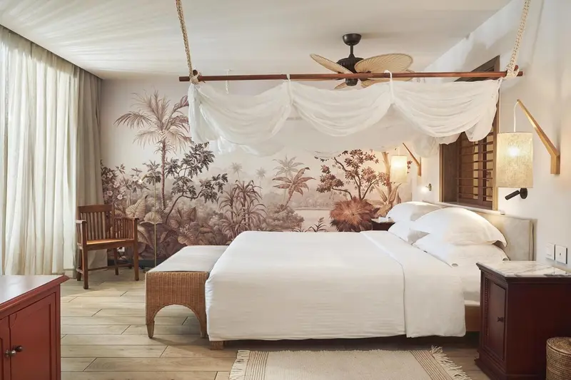 Une chambre lumineuse avec un grand lit à baldaquin et un décor tropical sur le mur.