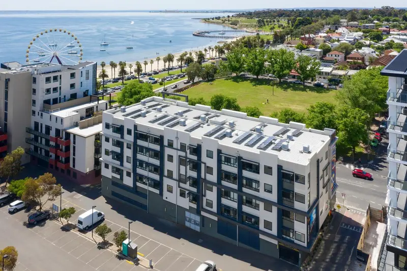 Vue aérienne d'un complexe immobilier moderne avec une pelouse verdoyante et la mer en arrière-plan.