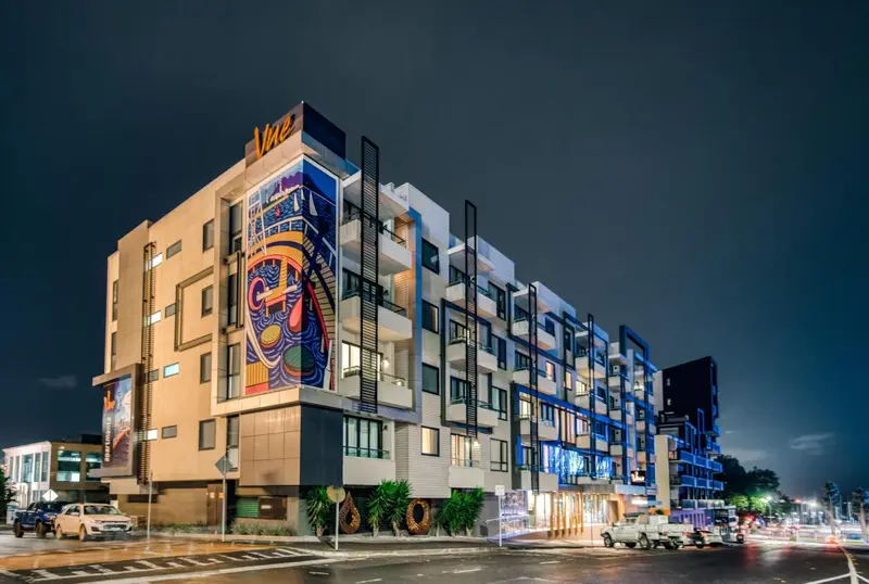 Façade moderne d'un bâtiment illuminé la nuit, avec une fresque colorée.