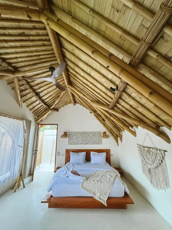 Une chambre lumineuse avec un lit recouvert de textiles blancs et un décor mural en fibres naturelles.