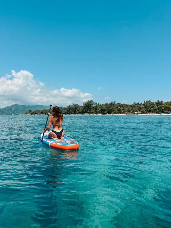Une personne pratique le paddleboard sur une eau turquoise face à une île verdoyante.