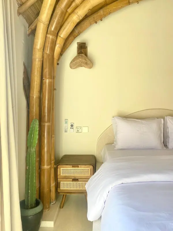 Une chambre lumineuse avec un lit recouvert de draps blancs et une décoration en bambou.