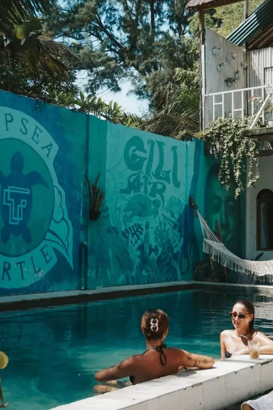 Deux personnes se détendent au bord d'une piscine turquoise devant un mur décoré.
